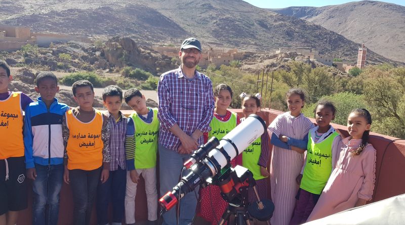 Mazin and ten schoolchildren pose by his telescope in the sun, with rugged mountains in the background