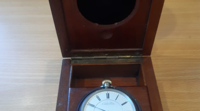 The watch, face-up, in a hinged wooden box