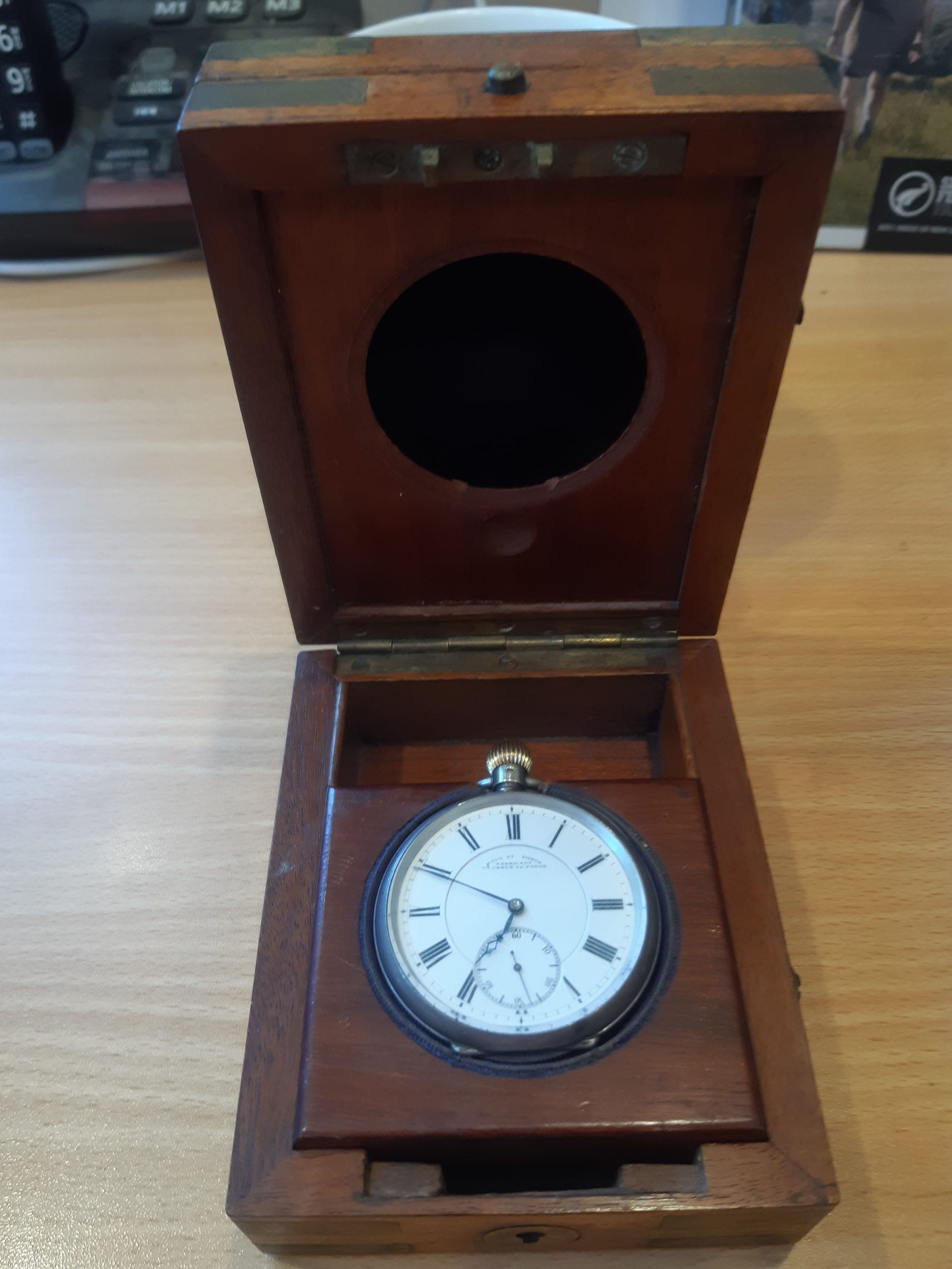 The watch, face-up, in a hinged wooden box