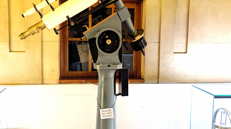 The white telescope tube is mounted on an equatorial mount upon a plinth.