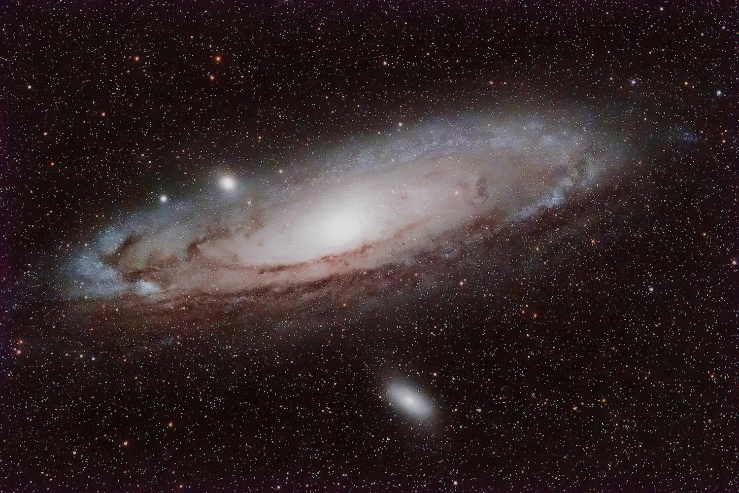 The bright foreshortened disc of the Andromeda Galaxy, with dust lanes visible in silhouette against its bright nucleus. Its much smaller satellite galaxy, M32, is also visible