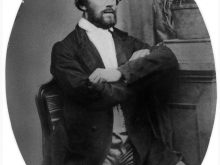 A photograph of the bearded Brorsen, sitting in a chair with arms folded
